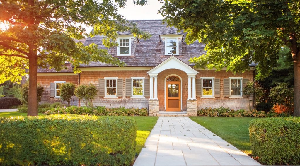 Coastal style home exterior at sunset with green trees and grass.